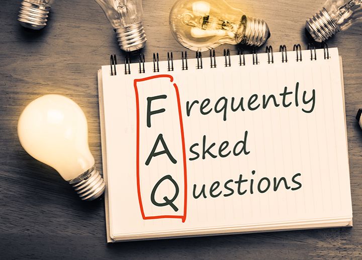 Notebook open to a page with ‘FAQ Frequently Asked Questions’ written beside lightbulbs on a desk